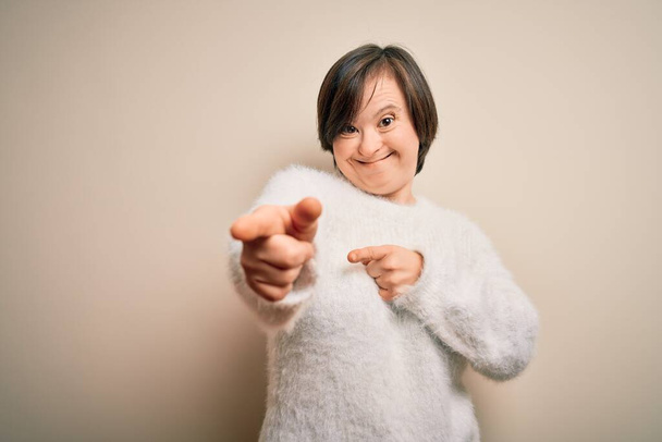 Молода вниз синдром жінка стоїть над ізольованим тлом, вказуючи пальці на камеру з щасливим і смішним обличчям. Хороша енергія і вібрує
. - Фото, зображення