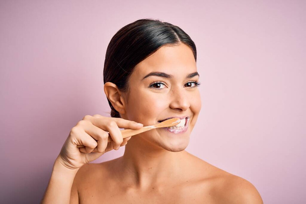 Νεαρή όμορφη μελαχρινή γυναίκα βουρτσίζει τα δόντια της χρησιμοποιώντας οδοντόβουρτσα και στοματική πάστα, τον καθαρισμό των δοντιών και της γλώσσας ως υγιεινή καθημερινή φροντίδα της υγείας - Φωτογραφία, εικόνα