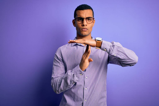 紫色の背景に縞模様のシャツと眼鏡を身に着けているハンサムなアフリカ系アメリカ人男性手でジェスチャーをします。 - 写真・画像