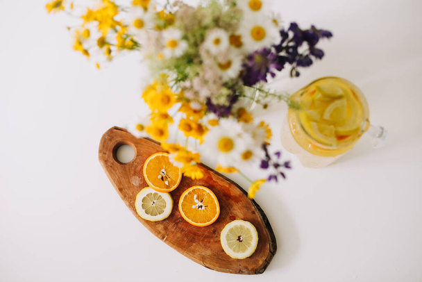 Summer concept. Wild flower bouquet on the table. Homemade lemonade with oranges and lemons. Healthy fresh beverage with citruses - Fotó, kép