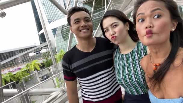 Three asian friends enjoying outdoor city life, taking selfies and making grimaces to the camera. Friendship and holiday concept - Footage, Video