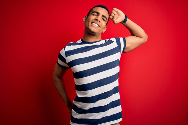 Handsome african american man wearing casual striped t-shirt standing over red background stretching back, tired and relaxed, sleepy and yawning for early morning - Fotografie, Obrázek