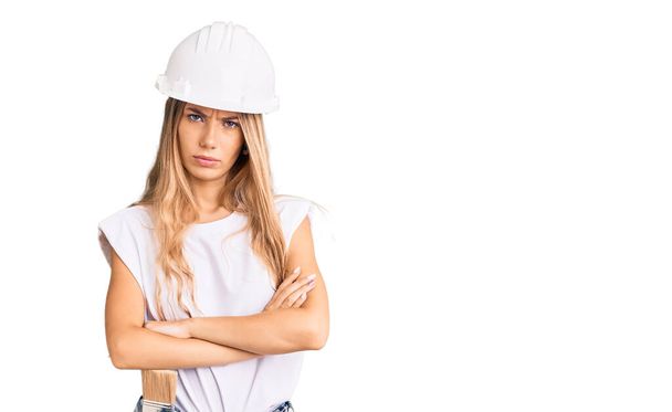 Beautiful caucasian woman with blonde hair wearing hardhat and painter clothes skeptic and nervous, disapproving expression on face with crossed arms. negative person.  - Foto, Imagem