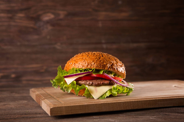 Burger on a wooden board on wooden table over dark background. - 写真・画像