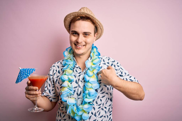 Young redhead tourist man on vacation wearing hat and hawaiian lei drinking cocktail pointing finger to one self smiling happy and proud - Photo, Image