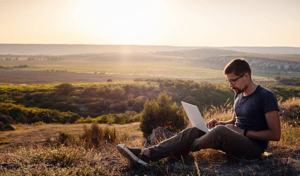 άνθρωπος με φορητό υπολογιστή κάθεται στην άκρη ενός βουνού με εκπληκτική θέα στην κοιλάδα. έννοια κάλυψης broaband δικτύου κινητής τηλεφωνίας. 5Ζ. - Φωτογραφία, εικόνα