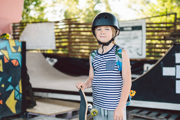 Παιδιά αγόρι με σκέιτμπορντ, διακοπές το Σαββατοκύριακο, εκπαίδευση, τα πρώτα βήματα στο πλοίο. Skateboarder αγόρι. Χαμογελώντας κομψό παιδί νεαρός κρατώντας πατινάζ σκάφους σε εξωτερικούς χώρους. παλικάρι κοιτάζοντας την κάμερα. - Φωτογραφία, εικόνα