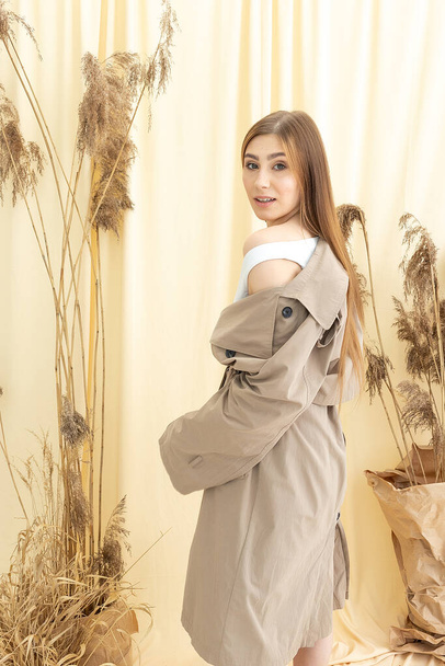 красивая женщина в бежевом плаще на фоне пастельной ткани. модная фотосессия
 - Фото, изображение