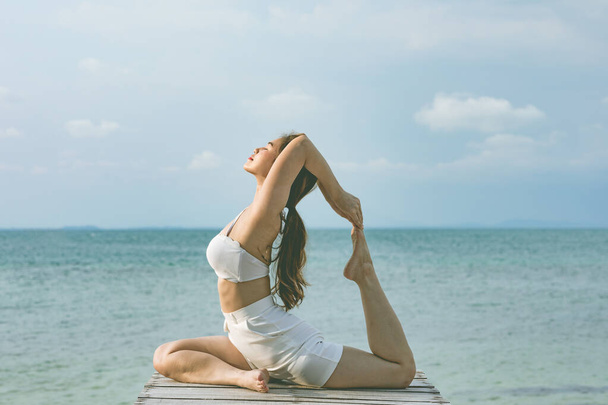 Vacances d'attrayant asiatique femme relaxant dans le yoga roi pigeon pose sur la jetée au-dessus de la plage avec belle mer dans l'île tropicale, Se sentir à l'aise et se détendre en vacances, Vacances Concept - Photo, image