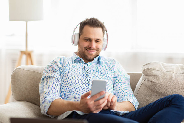 Happy man listening to music sitting on couch - Фото, зображення