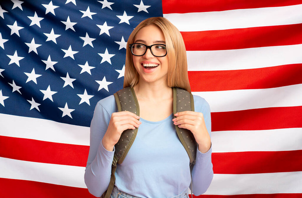 Étudier aux États-Unis. Happy Teen Girl avec sac à dos sur fond de drapeau américain - Photo, image