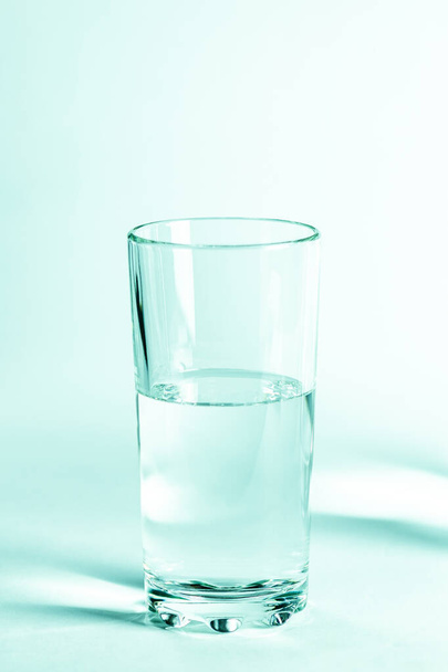 Glas mit klarem Wasser und Schatten auf weißem Hintergrund - Foto, Bild