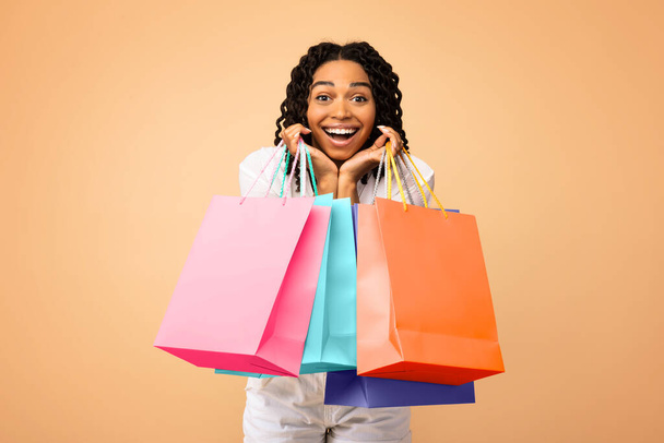 Mujer adicta a las compras emocionada sosteniendo bolsas en el fondo del estudio beige
 - Foto, imagen