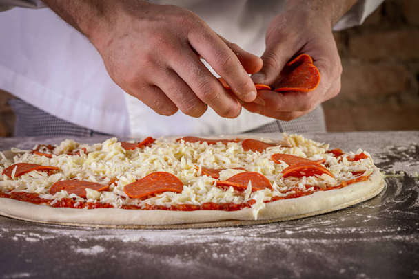 Fresh pizza dough being prepared with tomato sauce, mozzarella and pepperoni. The process of making pizza - Photo, Image