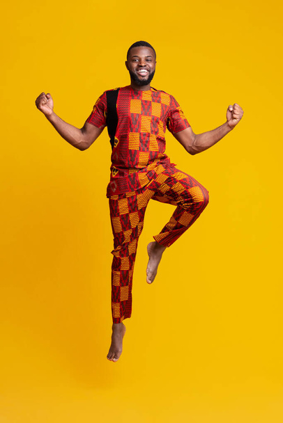 Excited black man jumping up over yellow background - Fotografie, Obrázek
