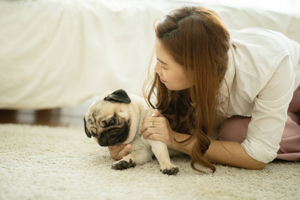 Beautiful Asian young woman playing with her pet and smile with dog pug breed looking in funny face in bedroom feeling so relax and comfortable,Friendly Concept - Foto, Imagem