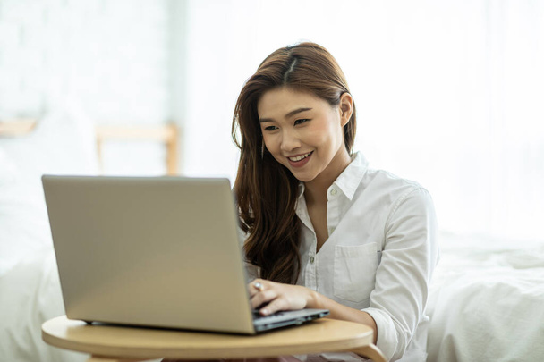 Lifestyle of Beautiful Attractive Asian woman smile working or shopping online with computer laptop in bedroom feeling so happiness and cheerful,Relax in holiday with laptop and using social network - Фото, изображение