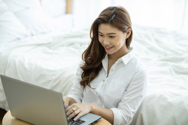 Lifestyle of Beautiful Attractive Asian woman smile working or shopping online with computer laptop in bedroom feeling so happiness and cheerful,Relax in holiday with laptop and using social network - Foto, imagen