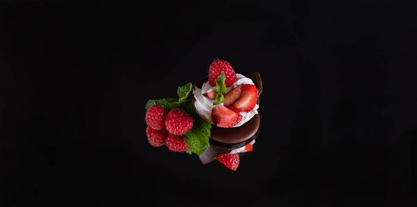 dessert of chocolate, whipped cream and fresh berries on a reflective surface, black background. the concept of a delicious summer holiday. selective focus. - 写真・画像