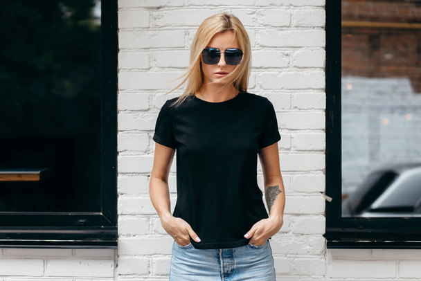 Menina loira elegante vestindo t-shirt preta e óculos posando contra a rua, estilo de roupa urbana. Fotografia de rua - Foto, Imagem