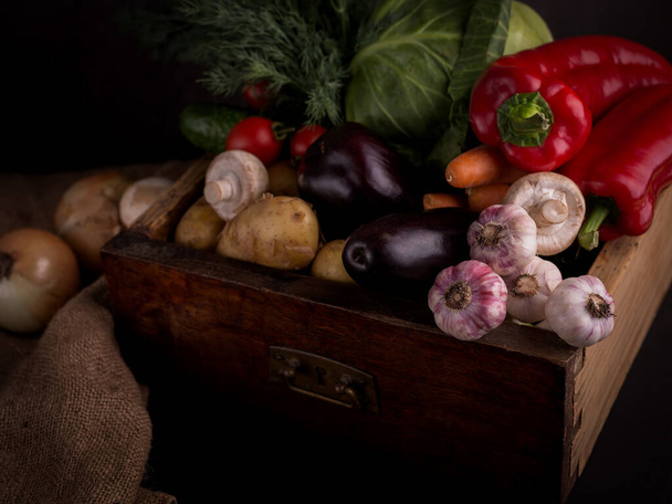 Assortment of fresh raw vegetables in a wooden box against black background. Healthy organic local food. - Photo, Image