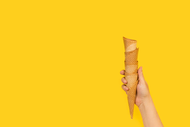 Woman hand holding a heap oh wafer cones on a yellow background with copy space - Valokuva, kuva