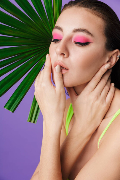 Photo closeup of seductive brunette woman posing with palm leaf isolated over violet background - Fotoğraf, Görsel