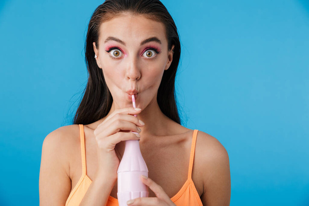 Photo of alluring shocked woman drinking soda from plastic bottle isolated over blue background - Fotografie, Obrázek
