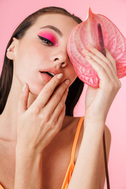 Photo closeup of brunette sexual woman posing with exotic flower isolated over pink background - Fotografie, Obrázek