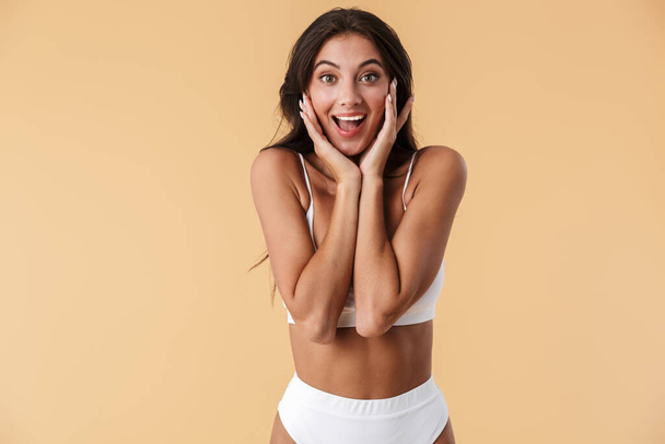 Image of a pretty happy surprised young woman in swimwear posing isolated over beige wall background. - 写真・画像