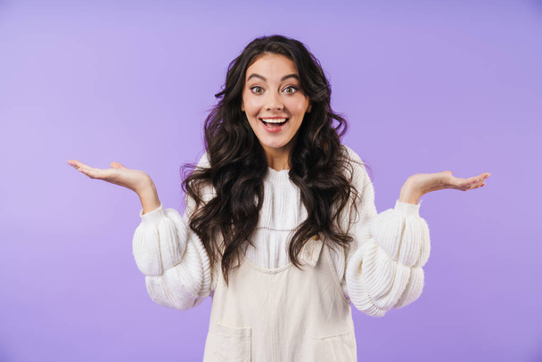 Photo of surprised young brunette woman posing isolated over purple wall background showing copyspace. - Photo, Image