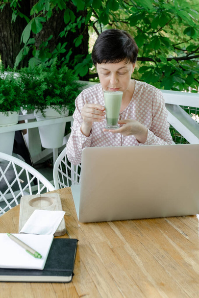 Mujer Freelancer o Blogger sentada en el lugar de trabajo con una taza de café o té verde Matcha tarde. Concepto de Alimentación Saludable en Período de Menopausia. - Foto, imagen