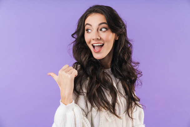 Photo of cheery emotional young brunette woman posing isolated over purple wall background pointing aside. - Photo, Image