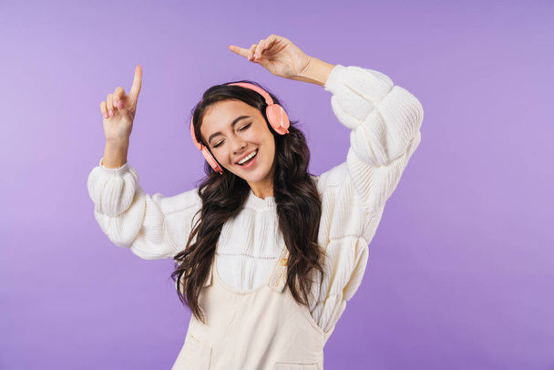 Photo of positive optimistic cheery brunette woman posing isolated over purple wall background listening music with headphones dancing. - Photo, Image