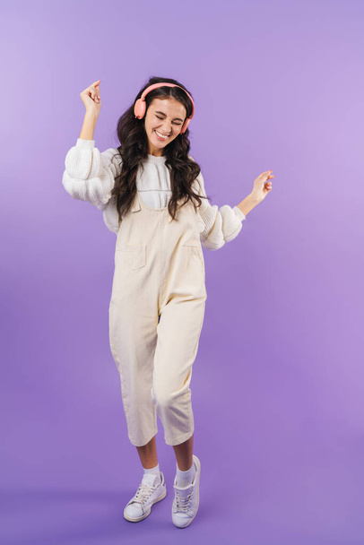 Photo of positive optimistic cheery brunette woman posing isolated over purple wall background listening music with headphones dancing. - Foto, Imagen