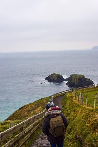 Photo of a young and attractive man with beard standing in the nature with winter clothes and a backpack in the Giants Causeway, Belfast. Holidays concept - Foto, imagen