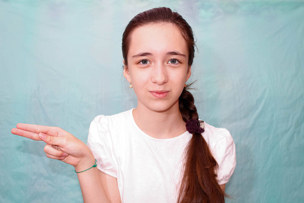 Dziewczyna z długim warkoczem pokazuje literę H używając języka migowego głuchych. Średni plan, turkusowe tło. - Zdjęcie, obraz