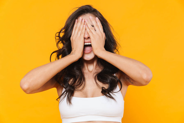 Image of scared young woman in swimsuit covering her face and screaming isolated over yellow wall - Foto, imagen