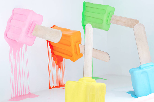 Fundo de verão mínimo criativo de manequins de sorvete de fusão coloridos na sala branca, picolés brilhantes em um pau. Luz e brilhantes pops de cor
 - Foto, Imagem