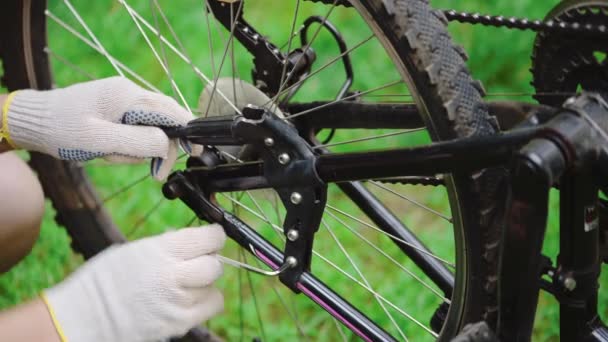Ένας ειδικός στην επισκευή ποδηλάτων με γάντια σφίγγει τις βίδες χρησιμοποιώντας ένα κλειδί allen στους πρόποδες ενός ποδηλάτου βουνού. Επείγουσα επισκευή οχήματος σε δρόμο μέσα σε δάσος το καλοκαίρι. Ενεργός τρόπος ζωής, καλοκαιρινά αθλήματα - Πλάνα, βίντεο