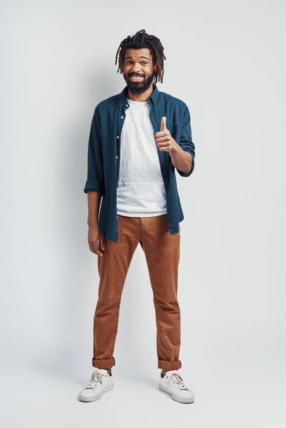 Full length of handsome young African man in casual wear smiling and showing thumb up while standing against grey background - Fotografie, Obrázek