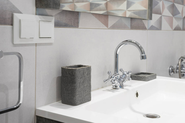 Interior de baño moderno con grifo de metal y fregadero blanco de cerámica. Accesorios de baño y espejo
. - Foto, imagen