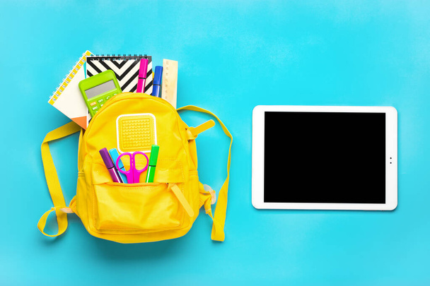 Retour à l'école, concept d'éducation. Sac à dos jaune avec fournitures scolaires Carnet, stylos, règle, calculatrice, ciseaux, tablette isolée sur fond bleu. - Photo, image