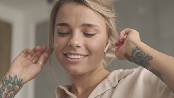 Fröhliche attraktive blonde Frau mit Kopfhörern, die zu Hause Musik hört und tanzt - Filmmaterial, Video