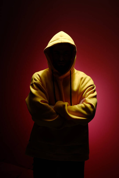 A young man of 25-30 years old in a yellow sweatshirt is standing against a red wall.  - Фото, изображение