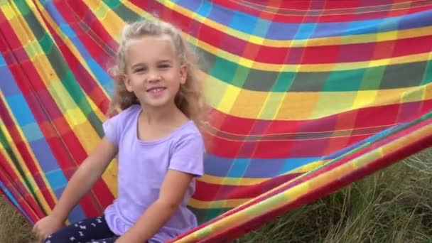 Happy little girl swinging in colorful hammock, summertime joy on backyard - Záběry, video