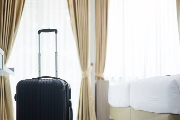 Černá zavazadla v moderním hotelovém pokoji s okny, záclonami a pozadím postele. Čas na cestování, relaxaci, cestu, výlet a dovolenou koncepty - Fotografie, Obrázek