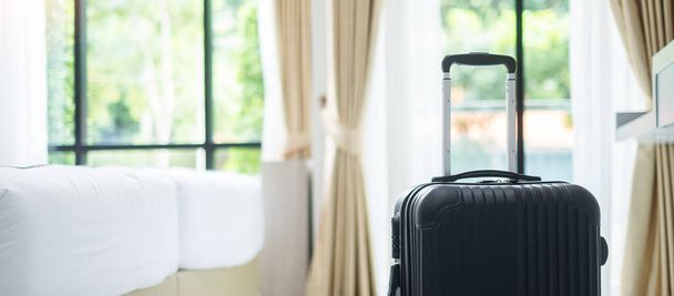 Czarny Bagaż w nowoczesnym pokoju hotelowym z oknami, zasłonami i łóżkiem na zielonym tle natury. Czas podróży, relaksu, podróży, podróży i wakacji koncepcje - Zdjęcie, obraz