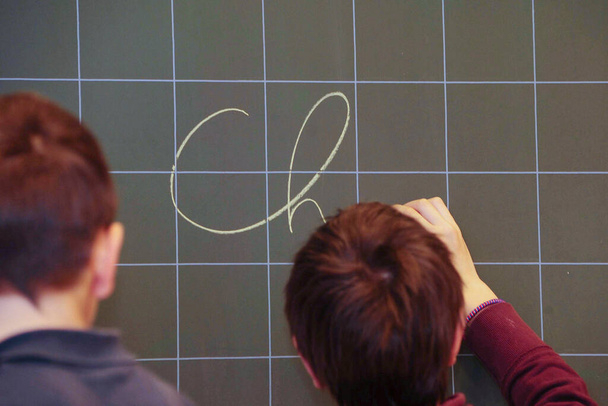 μαθητής στο δημοτικό σχολείο γράφει με κιμωλία στον πίνακα - Φωτογραφία, εικόνα