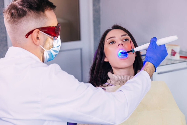 Διαδικασία λεύκανσης δοντιών με τη χρήση ειδικής συσκευής με υπεριώδη λάμπα. Ασθενής σε οδοντιατρική καρέκλα. - Φωτογραφία, εικόνα